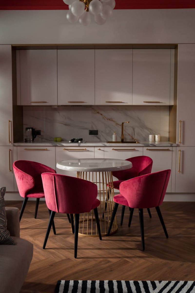 Cozy kitchen interior with pink velvet chairs, a round table, and modern cabinetry.